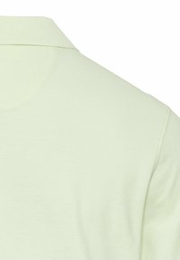 Gros plan sur le col et l'épaule d'une chemise en tissu vert clair avec des coutures visibles et une texture tricotée.
