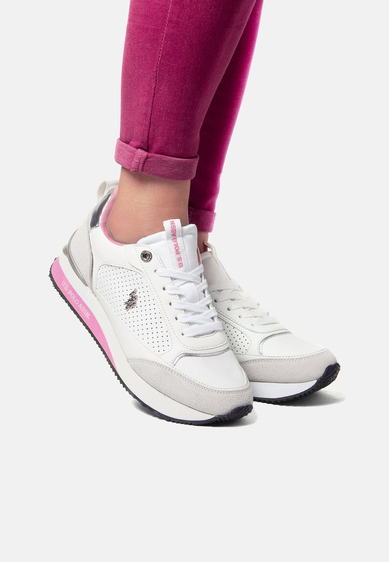Bílé a šedé tenisky s růžovými akcenty, perforovaný svršek, texturované překryvy, ploché tkaničky a gumová podrážka s vzorovaným běhounem.