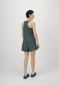 Teal värvi sportlik tank top ja lühikesed püksid, valmistatud kergest kangast. Omab rihma seljaosa disaini ja külgvahesid paindlikkuse tagamiseks. Jalatsid on mustad teal aktsentidega.