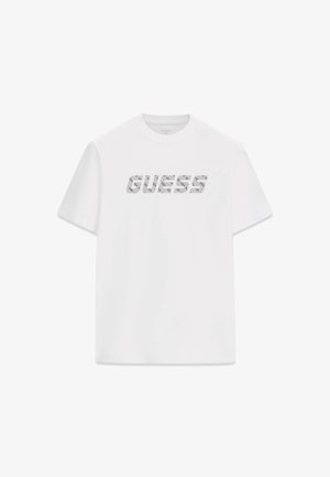 T-shirt en coton blanc avec le mot « GUESS » dans un design graphique à texture imprimée, manches courtes et col rond.