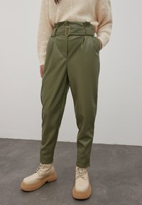 Olijfgroene, hoog-waist broeken van faux leer. Voorzien van een riem met een gouden gesp, zijzakken en taps toelopende benen.