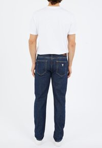 Dark blue denim jeans with a straight-leg fit, visible stitching, and back pockets. Worn with a plain white t-shirt and light sneakers.