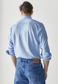 Vaalea sininen pitkähihaisen paidan, jossa on pehmeä tekstuuri, yhdistetty korkeavyötäröisiin farkkuihin, joissa on ruskea nahkapaikka takana.