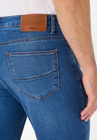 Blauwe denim jeans met een leren taillepatch, achterzakken met stikseldetails en een getailleerd ontwerp. Glad textuur, casual stijl.