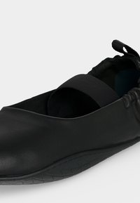 Μαύρο παπούτσι slip-on με ελαστικό λουράκι στο πάνω μέρος, ανάγλυφη σόλα και συλλεγμένη θηλιά στη φτέρνα για εύκολη χρήση.