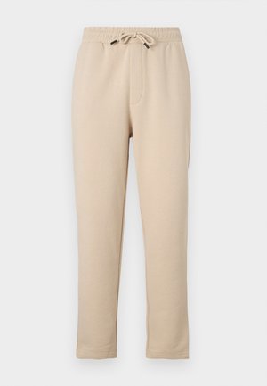 Beige sweatpants with elastic waistband, adjustable drawstring, two side pockets, and tapered leg design. Soft texture, casual style.