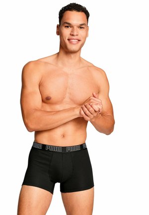 Boxer neri attillati, con un elastico in vita ben visibile contrassegnato dalla scritta "PUMA" in lettere bianche. Il modello è in piedi con le mani unite.