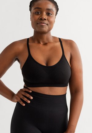 Zwarte sportbeha met dunne bandjes, een brede elastische band en een gladde textuur. Gecombineerd met hoge zwarte leggings.