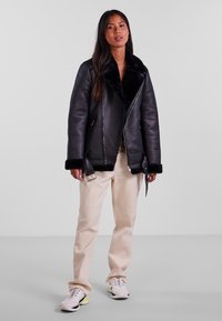 Black leather jacket with a faux shearling collar, zip closure, and contrasting black cuffs. Worn over light beige pants and white sneakers.