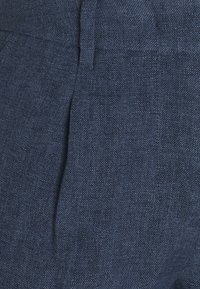 Pantalon en lin bleu foncé avec une finition texturée, doté de plis à l'avant et d'une taille plate pour un look sur mesure.