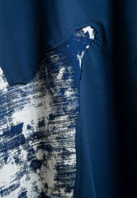 Tejido de color azul oscuro con un parche abstracto texturizado en blanco y azul cosido en él, con bordes irregulares y costuras visibles.