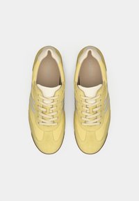 Ζευγάρι κίτρινων αθλητικών παπουτσιών με κορδόνια, με μπεζ λεπτομέρειες και ανοιχτό καφέ σόλες, σε λευκό φόντο, φωτογραφημένα από πάνω.