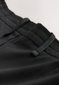 Shorts de sport noirs avec une taille élastique, un cordon de serrage et une texture de tissu lisse. Comprend des détails de couture discrets le long de la taille.