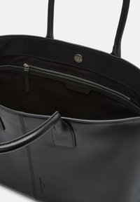 Sac fourre-tout en cuir noir avec une texture lisse, deux poignées robustes et une poche intérieure zippée. Doté d'une fermeture à pression en haut.