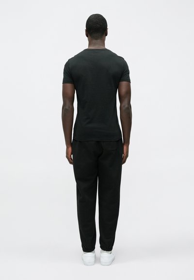 Fekete, rövid ujjú póló és hozzáillő tréningnadrág, mindkettő tömör pamut anyagból. A tréningnadrágnak elasztikus passzéja és oldalsó zsebei vannak. Fehér sportcipő.