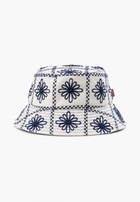Cappello a secchiello realizzato in tessuto crema con ricami floreali navy in un motivo a griglia. Corona rotonda e piatta e ampia visiera inclinata verso il basso.