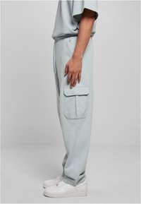 Light blue sweatpants made of soft fabric, featuring a side cargo pocket and an elastic waistband. Worn with white sneakers.