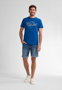 Modré bavlněné tričko s potiskem v světle zelené barvě. V kombinaci s vyhrnutými denimovými šortkami a bílými teniskami. Jednoduchý a ležérní design.