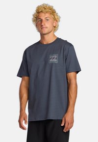 Navy blue cotton t-shirt featuring a front chest logo design in a lighter shade, short sleeves, and a round neckline. Simple, casual fit.
