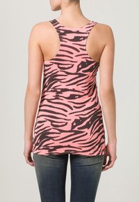 Débardeur rose avec un motif zèbre noir, doté d'un dos nageur et d'une coupe décontractée, associé à un jean foncé.