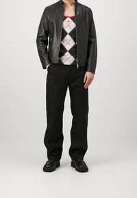 Black leather jacket with a high collar, worn over a multicolored argyle sweater and black loose-fitting pants, paired with chunky black shoes.
