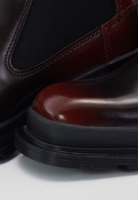 Bottes en cuir marron et bordeaux à finition lisse, avec des panneaux élastiques noirs texturés et des semelles en caoutchouc présentant un motif côtelé.