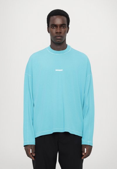 Light blue long-sleeve shirt with crew neck and white "BONSAI" text centered on the chest. Features relaxed fit and visible stitching details.
