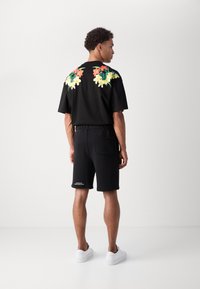 Chemise noire à manches courtes avec broderie florale au dos, associée à un short noir et des baskets blanches, offrant une coupe décontractée.