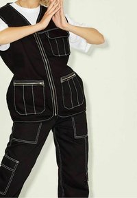 Svart ärmlös arbetsväst och matchande byxor med vit söm. Har flera fickor och dragkedja fram. Slät tygkvalitet.