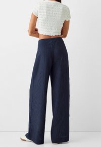 Marine-randiga vida byxor med hög midja, texturerad tyg och avslappnad passform. Tillsammans med en vit kort topp.