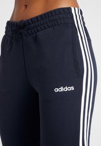 Marinblå sportiga joggers med dragsko i midjan, vit tre-stripes design på sidorna och en vit adidas-logotyp.