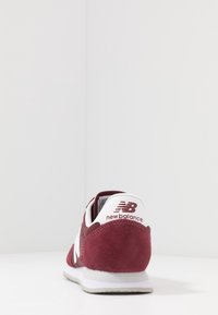 Baskets en suède rouge avec accents blancs, dotées d'une pointe arrondie, d'un col rembourré et d'une semelle en caoutchouc texturée. Marquage distinctif sur le talon.