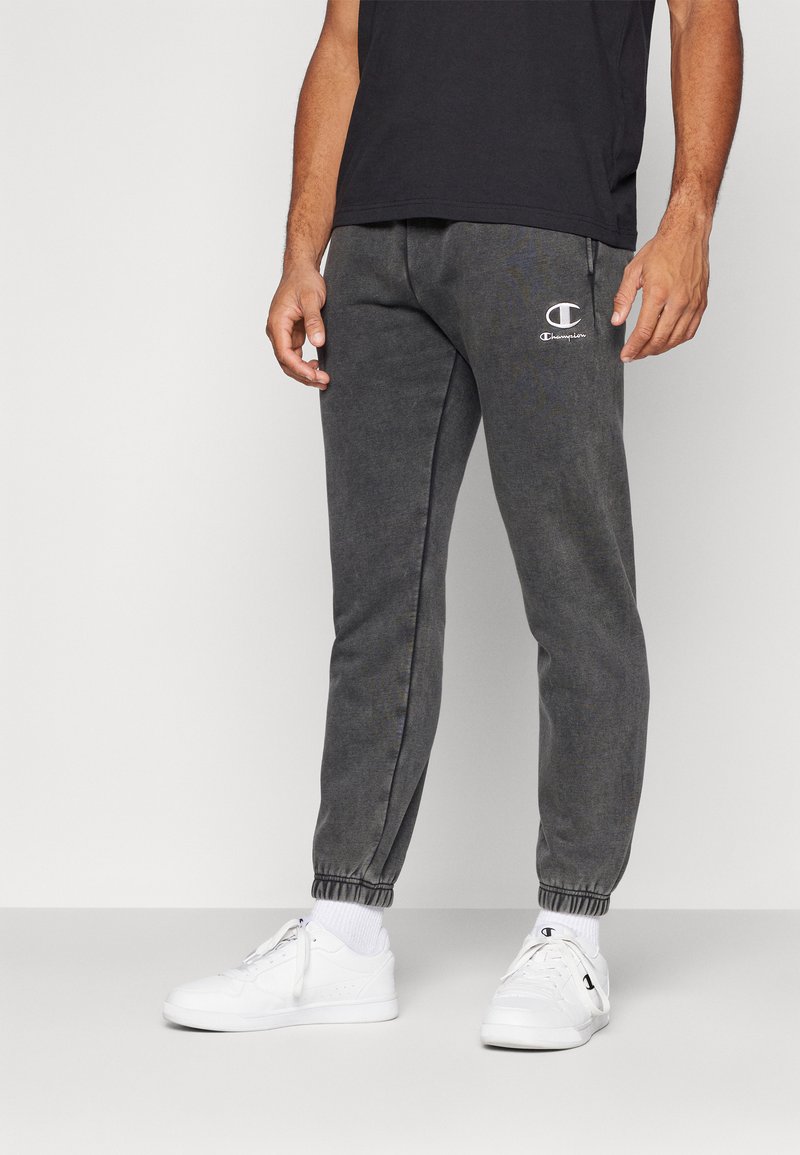 Grå sweatpants med elastiske mansjetter, snor i midjen, og en hvit brodert logo på venstre side. Glatt stofffinish.