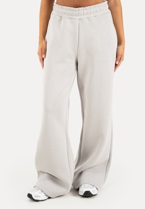 Løse lysegrå joggebukser med elastisk taljebånd båret med hvide sneakers på en stående person mod hvid baggrund.