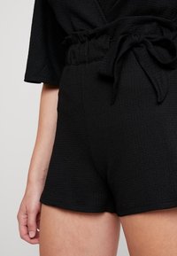 Shorts noirs texturés avec une ceinture à nouer et une coupe ample. Le tissu présente un motif subtil et un design décontracté.