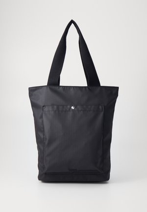 Schwarze Tragetasche mit breiten Stoffgriffen, Vordertasche mit silbernem Druckknopf gesichert, vor schlichtem hellem Hintergrund.