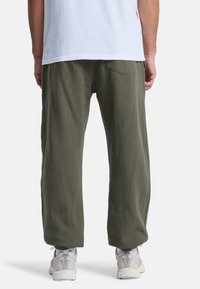 Olivgrön, löst sittande byxor i mjukt tyg, med en bakficka och som smalnar av mot botten, i kombination med ljusa sneakers.