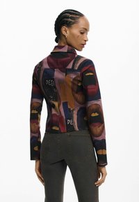 Top cu mânecă lungă, decorat cu un model colorat de buze. Confecționat dintr-un material neted și elastic. Design fără spate, cu guler înalt.