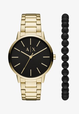 Reloj de metal dorado con una esfera redonda negra, marcadores dorados y una pulsera de eslabones. Acompañado de una pulsera de cuentas negras.