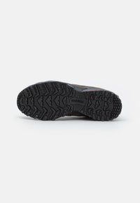 Fekete, strapabíró talpú New Balance túracipő mély barázdákkal a tapadás érdekében, egy fehér háttér előtt látható.