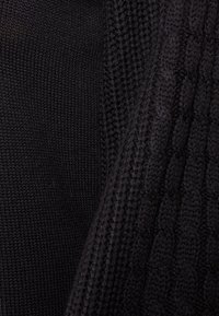 Tissu noir tricoté présentant une zone lisse et un motif côtelé texturé, avec des variations d'épaisseur créant un intérêt visuel.