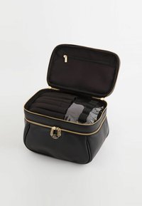 Sort zippered tas med guldfarvet hardware; interiøret har rum med sort stof og en gennemsigtig sektion til organisering.