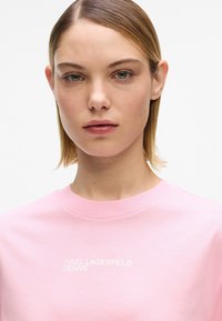 Roosa puuvillane t-särk ümar kaelusega, rinnal valge "KARL LAGERFELD JEANS" logo. Sile tekstuur ja lõdvestunud istuvus.