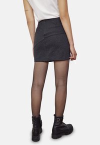 Jupe mini grise à rayures, avec une taille ajustée, associée à des collants en résille noirs et des bottines à boucles avec des semelles robustes.
