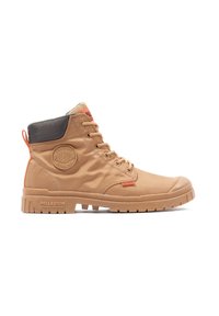 Tan ankle boots made of durable material, featuring a round logo patch, orange accents, and a textured rubber sole with deep treads.