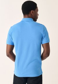 Világoskék póló, egyenes szegéllyel és rövid ujjakkal, puha anyagból készült. Gallérral és oldalsó hasítékokkal az alján.