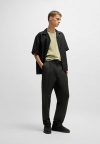 Chemise noire à manches courtes sur un t-shirt vert clair, associée à un pantalon sombre et des baskets noires ; comprend un collier en perles.