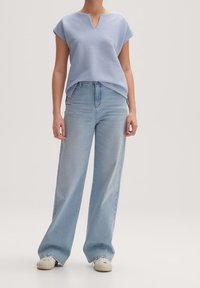 Světle modrý žebrovaný top s výstřihem do V, doplněný širokými světle modrými džíny a bílými teniskami, vytvářející uvolněný outfit.