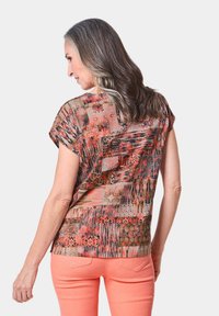 T-shirt a maniche corte con motivi vivaci in tonalità arancione, rosa e marrone; presenta una vestibilità ampia e un tessuto testurizzato per un effetto sovrapposto.