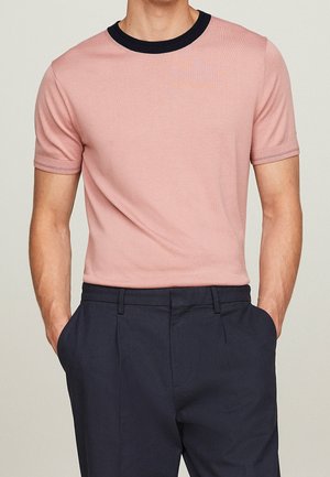 T-shirt z krótkim rękawem w różowym kolorze z bawełny, z granatowym ściągaczem przy dekolcie i rękawach, zestawiony z ciemnogranatowymi spodniami.